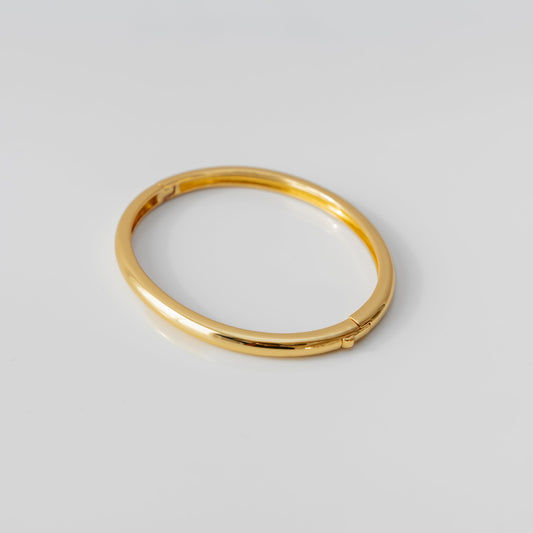 Gold bangle bracelet on a light gray background