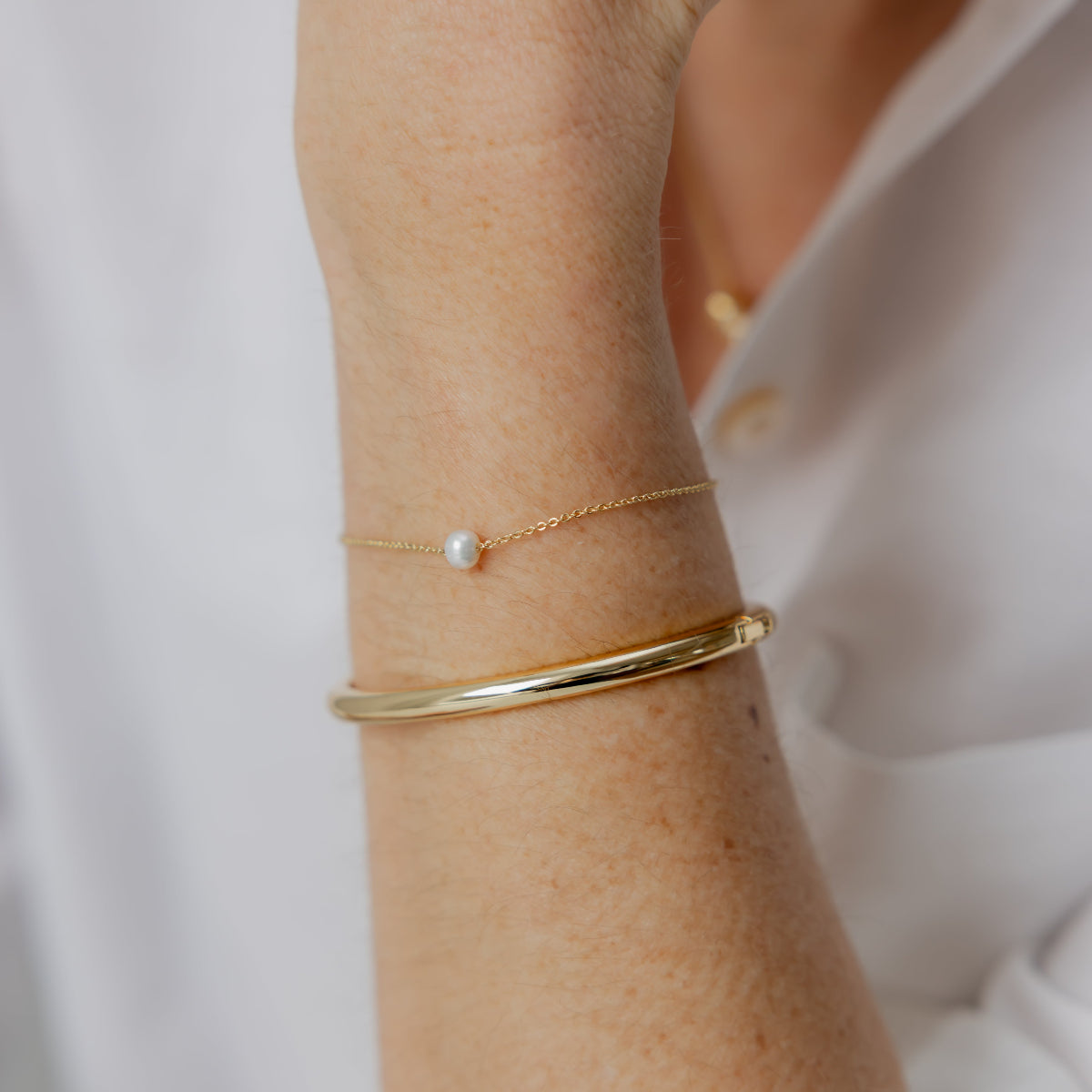 Close-up of a person's wrist wearing gold bracelets with a white background