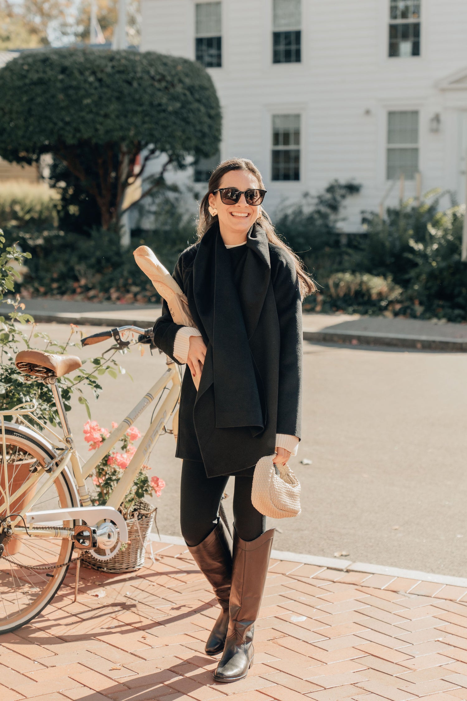 Woman in black outfit with sunglasses standing next to a bicycle outdoors for the holidays in her festive earrings