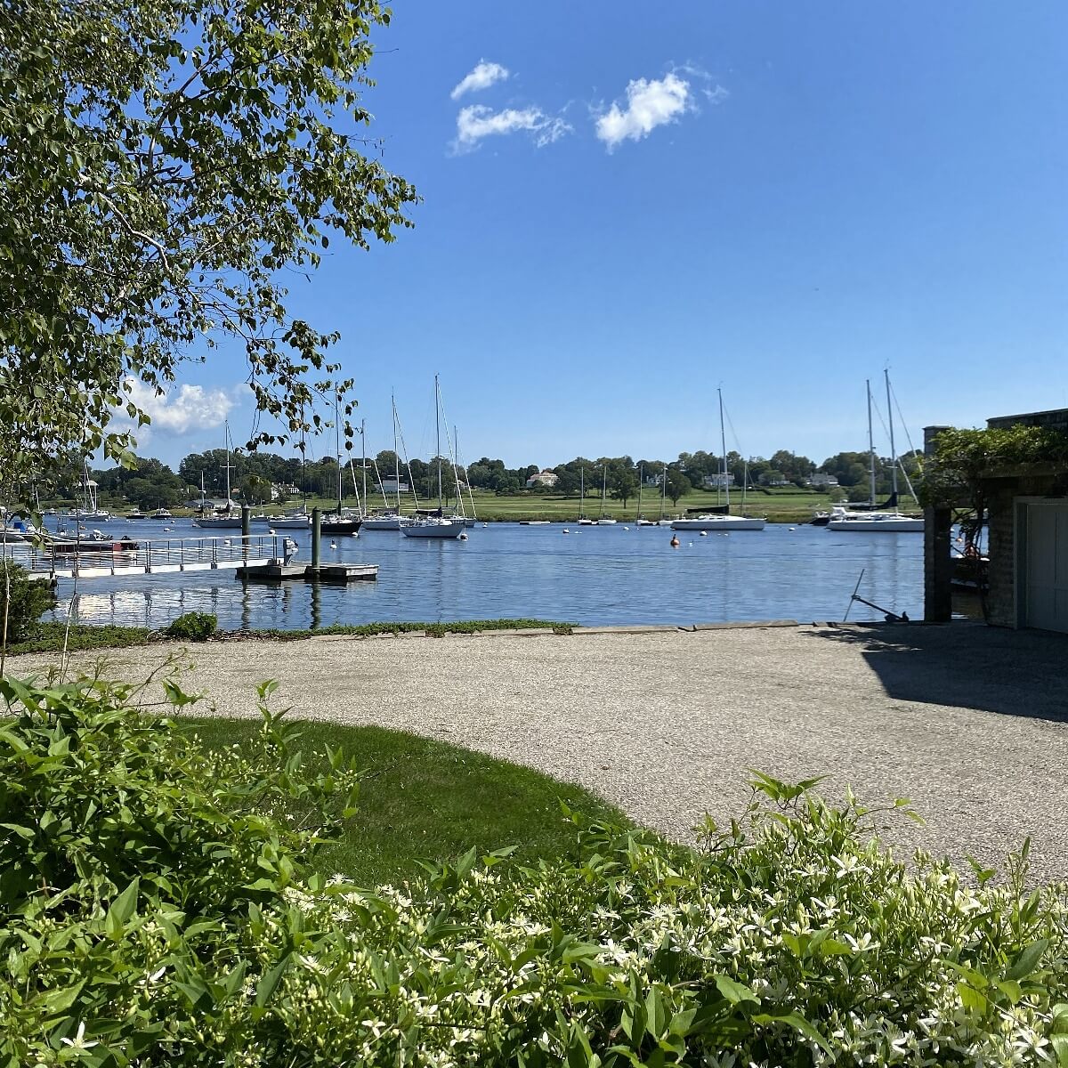 New England, old money, timeless heritage brand with Marina with sailboats on a clear day, surrounded by greenery and a gravel path.