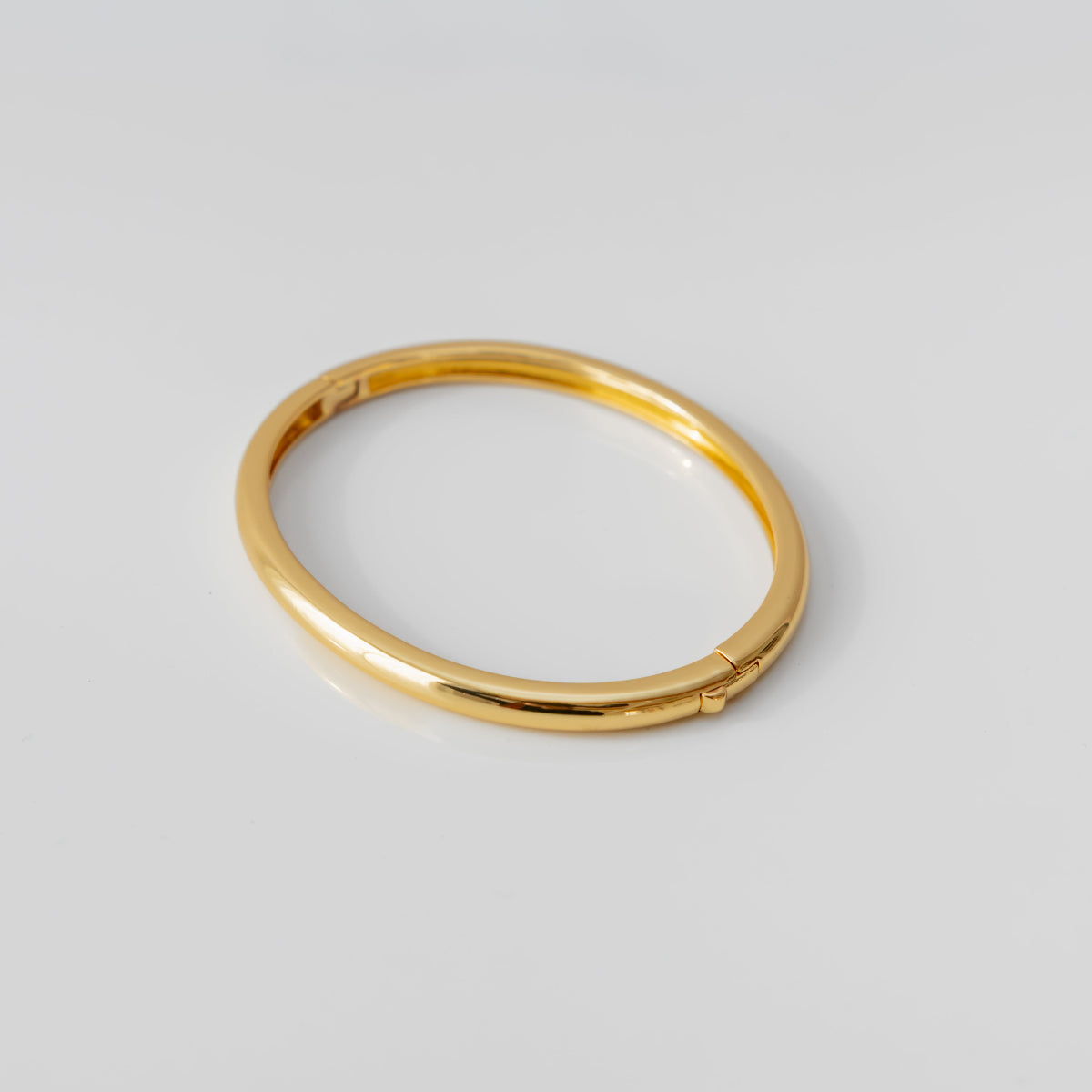 Gold bangle bracelet on a light gray background