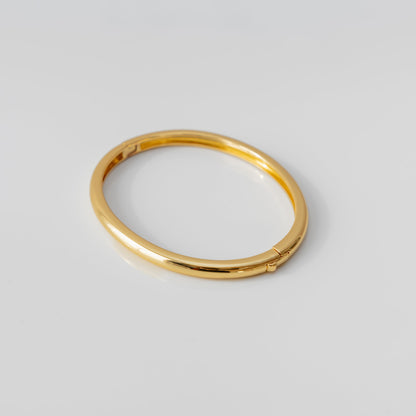 Gold bangle bracelet on a light gray background