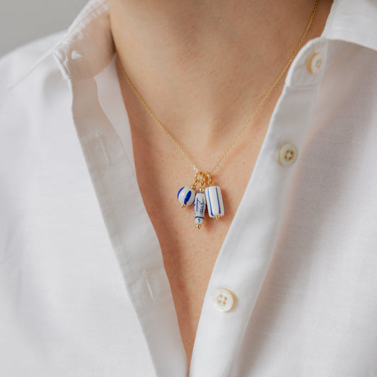 Necklace with three charms worn by a person in a white shirt.