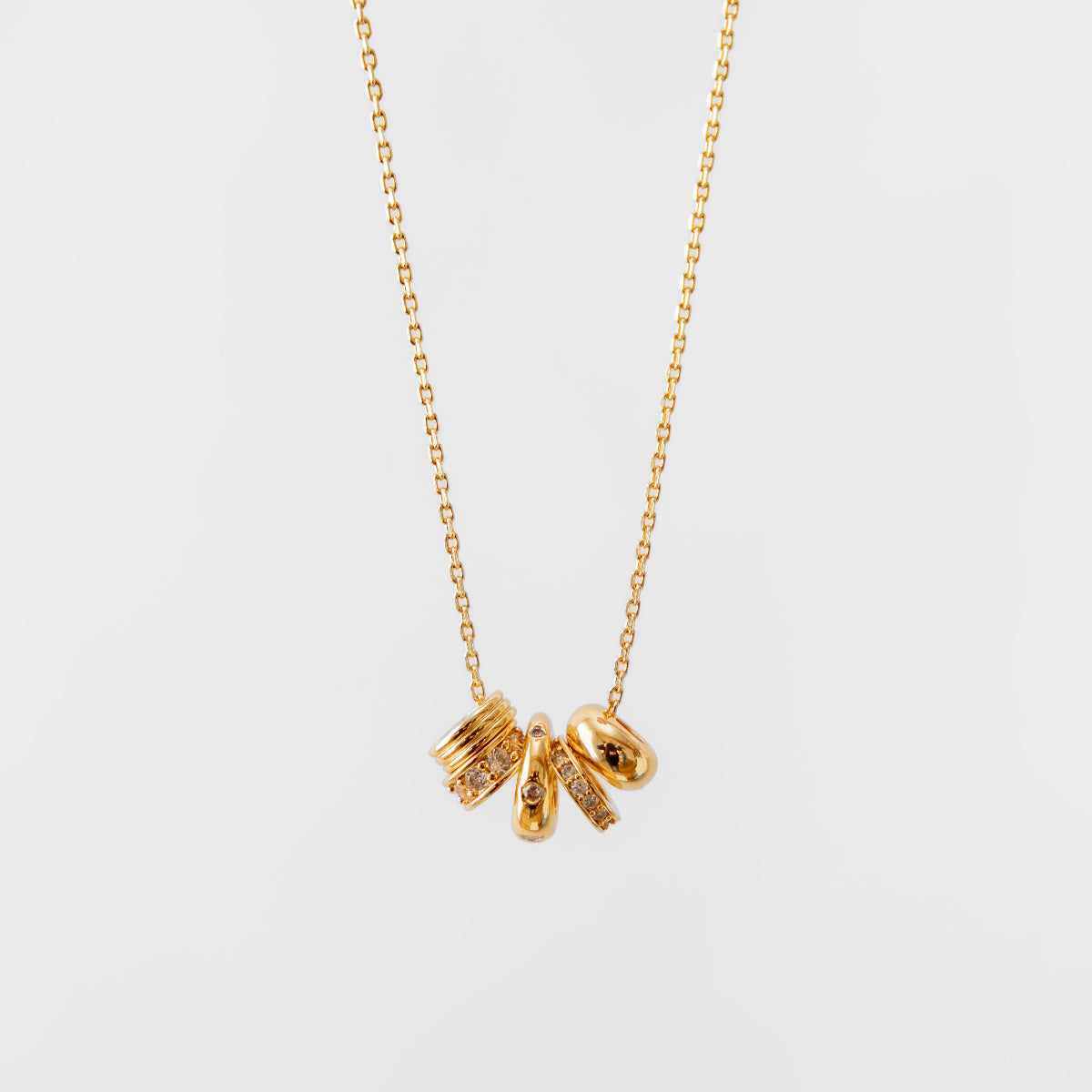 Gold charm necklace with three small pendants on a light gray background