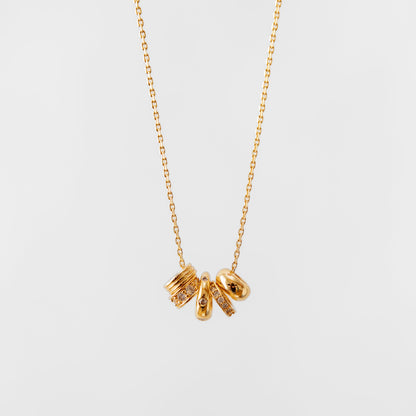 Gold charm necklace with three small pendants on a light gray background