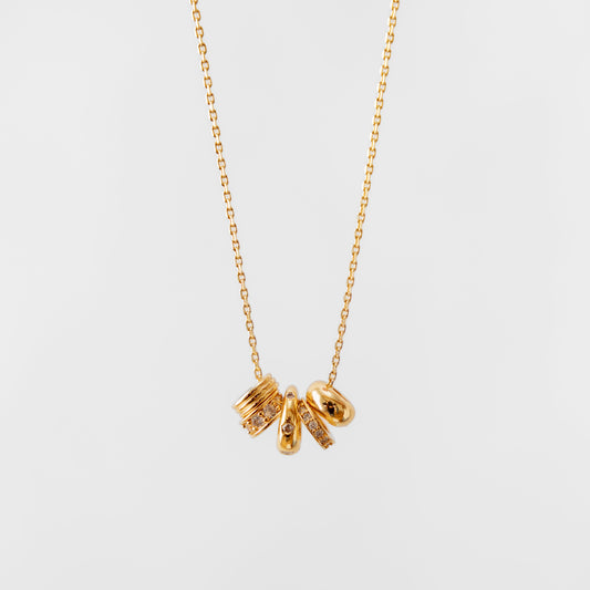 Gold charm necklace with three small pendants on a light gray background