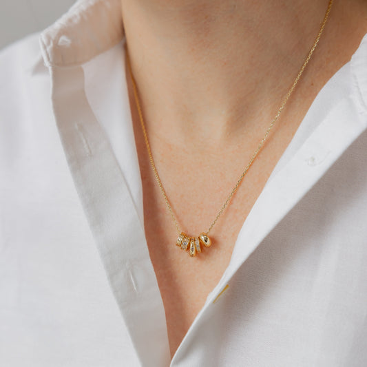 Gold necklace with a small pendant worn by a person in a white shirt.