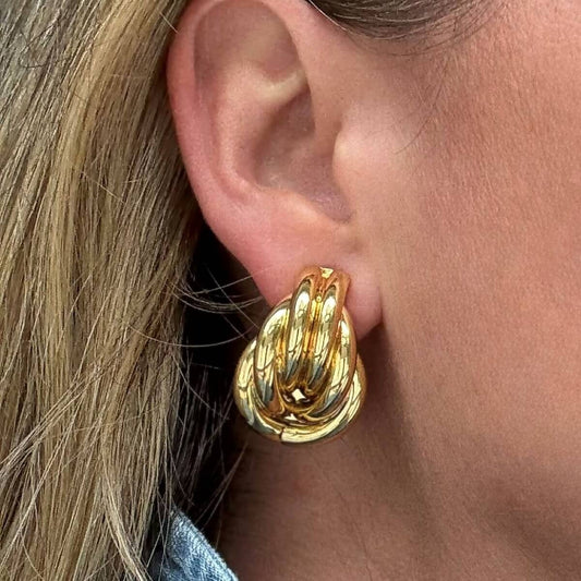 Gold knot earring worn by a person with blonde hair.