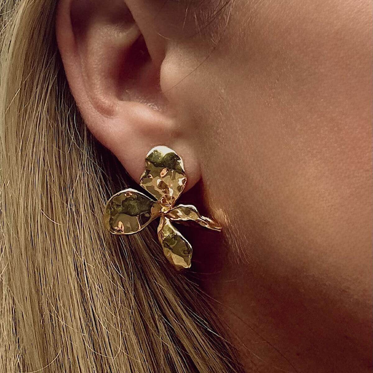 Gold flower earring worn by a person with blonde hair.