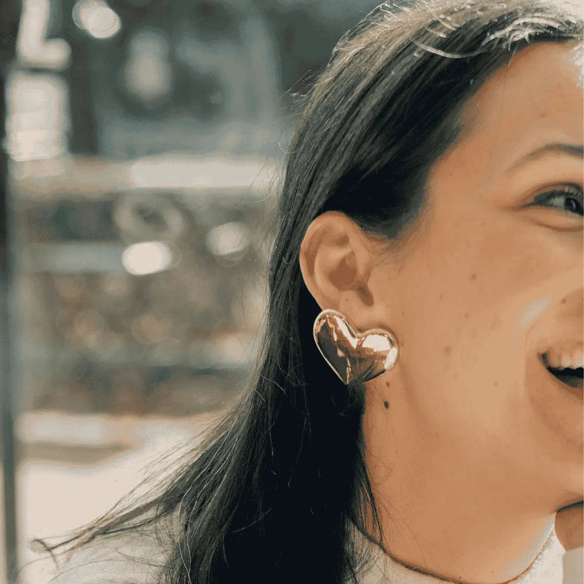 Gold heart-shaped earring worn by a person withbrownhair.
