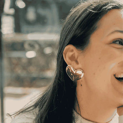 Gold heart-shaped earring worn by a person withbrownhair.
