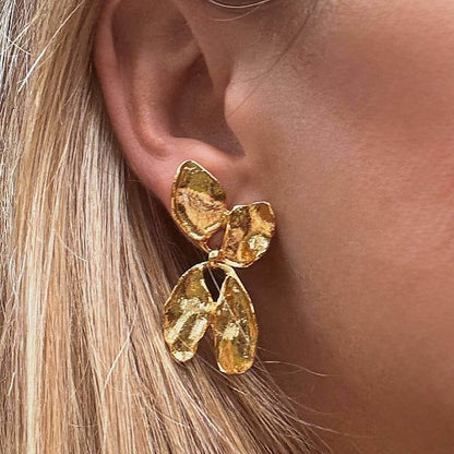 Gold flower petal earring worn by a person with blonde hair.