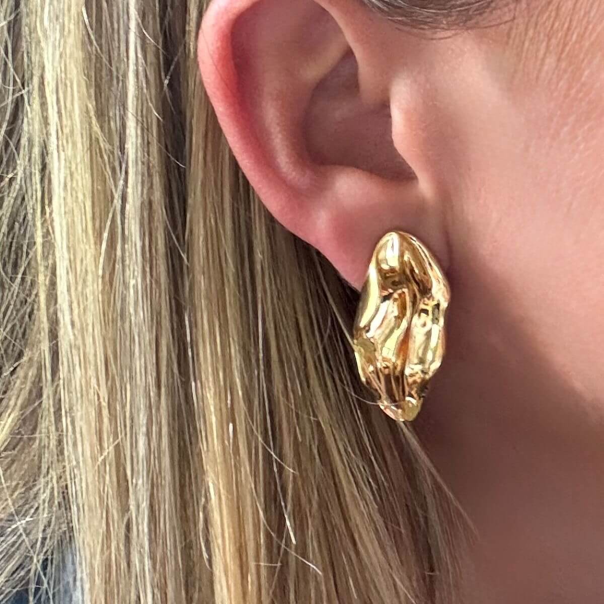 Gold wave earring worn by a person with blonde hair.