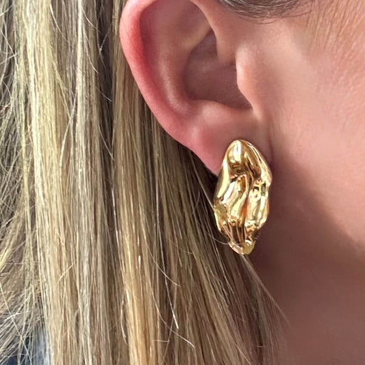 Gold wave earring worn by a person with blonde hair.