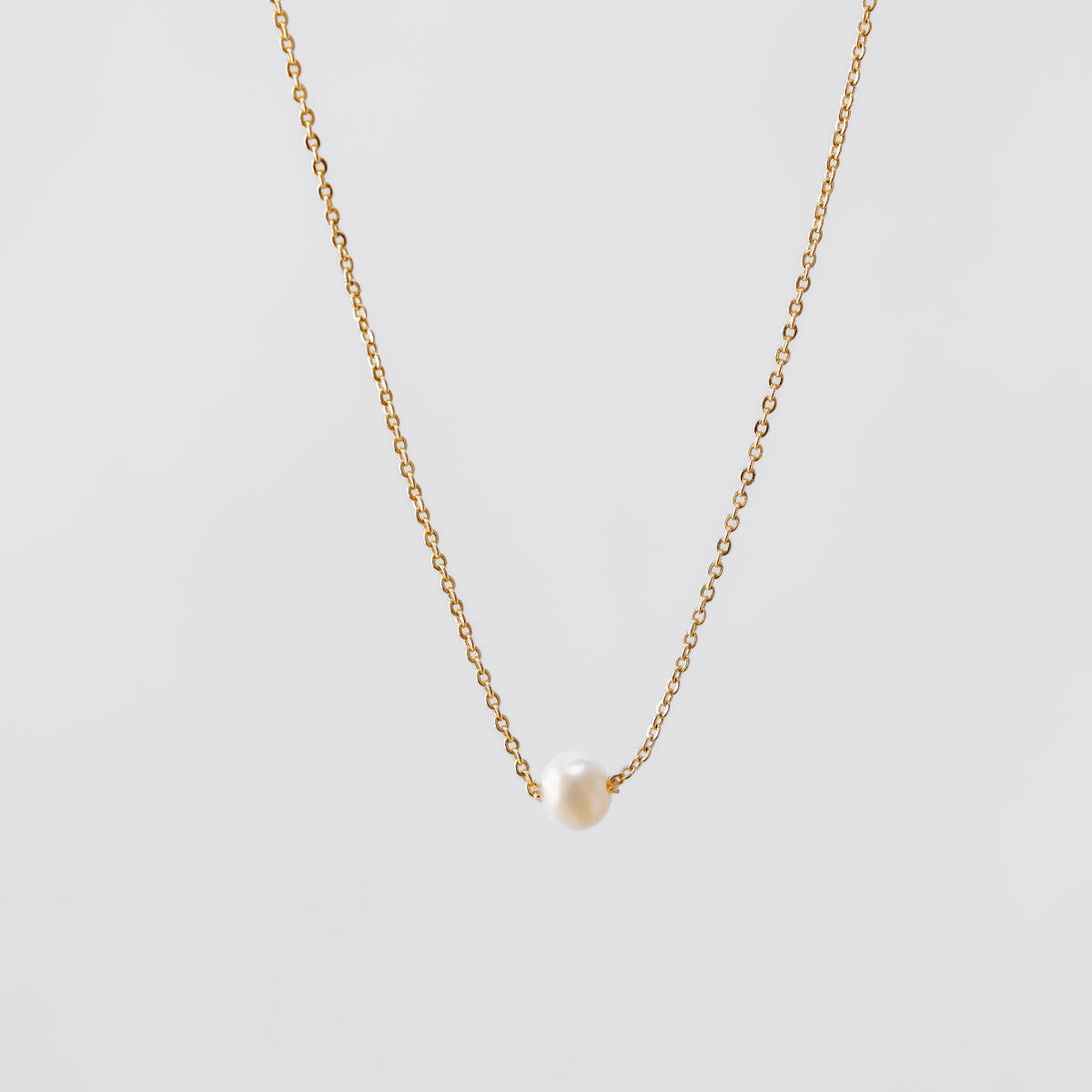 Gold pearl necklace with a small pendant on a light gray background