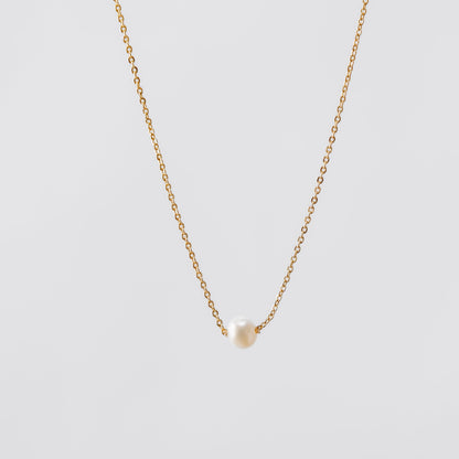 Gold pearl necklace with a small pendant on a light gray background