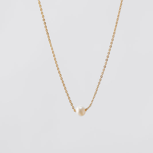 Gold pearl necklace with a small pendant on a light gray background