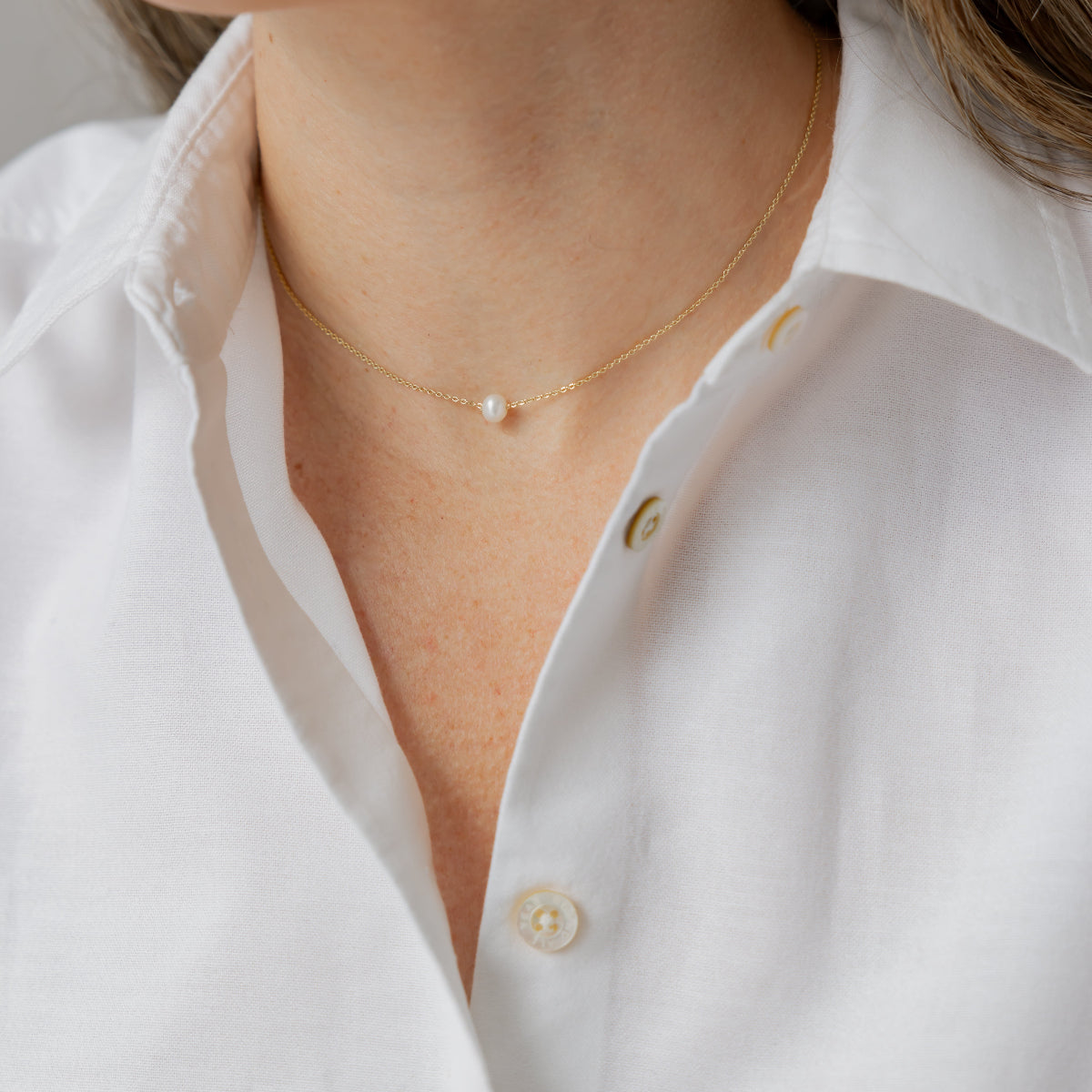 Close-up of a person wearing a white shirt and pearl necklace.