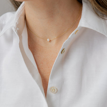 Close-up of a person wearing a white shirt and pearl necklace.
