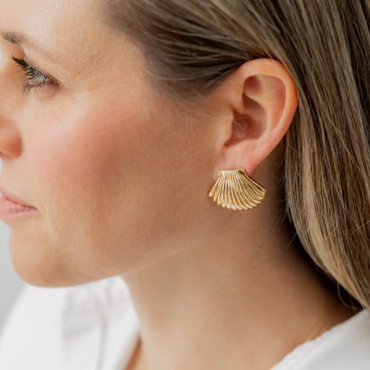 Close-up of a person wearing gold earrings with a white shirt in the background