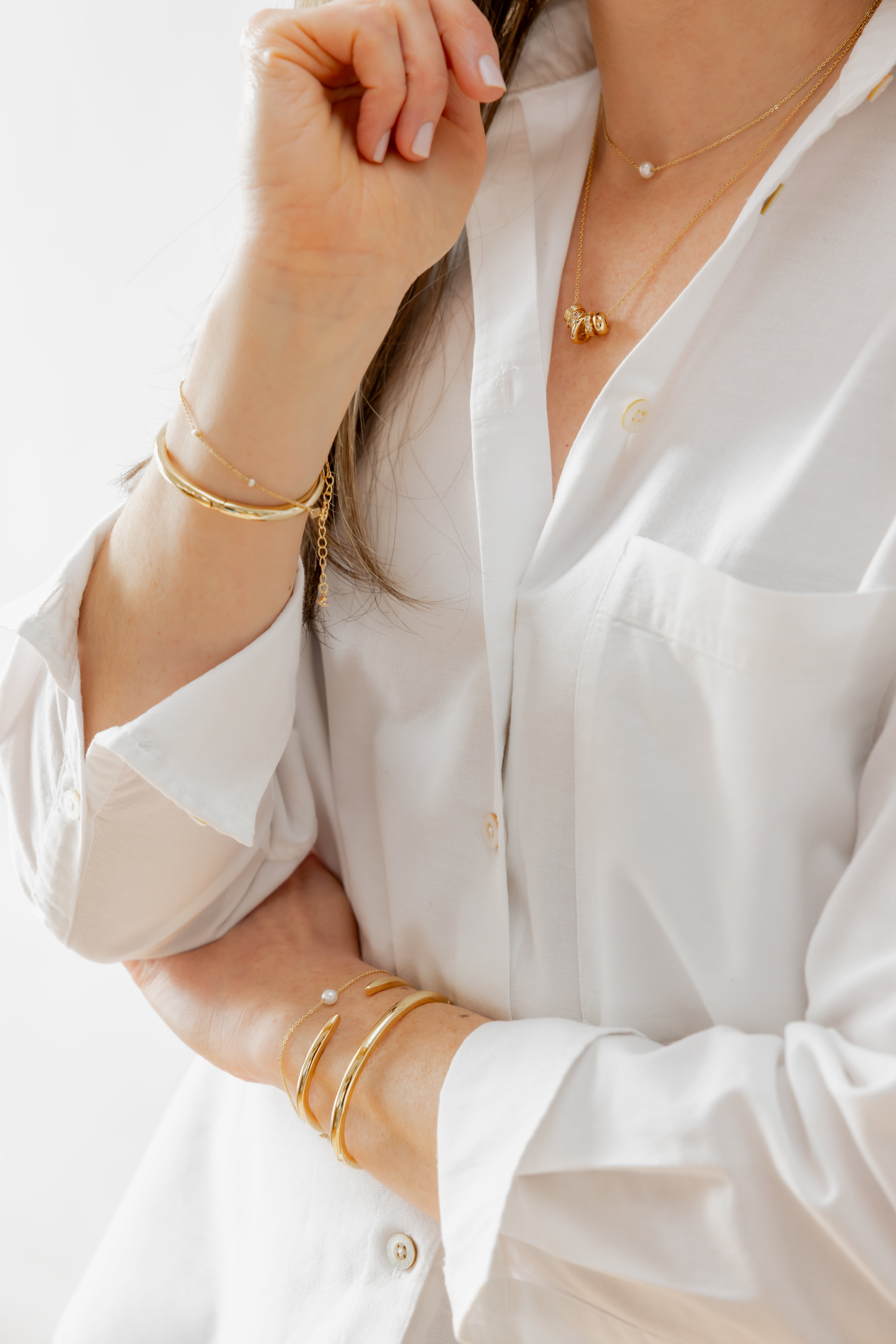 Close-up of a person wearing a white shirt with gold jewelry on a light background